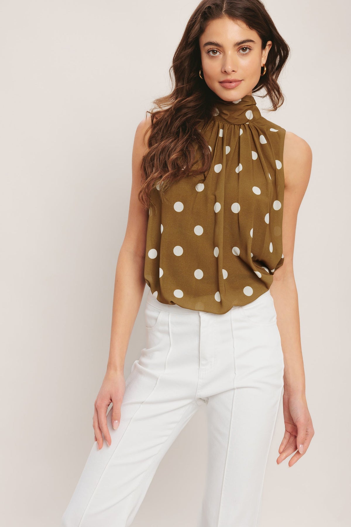 Woman wearing a polka dot blouse and white pants against a plain background
