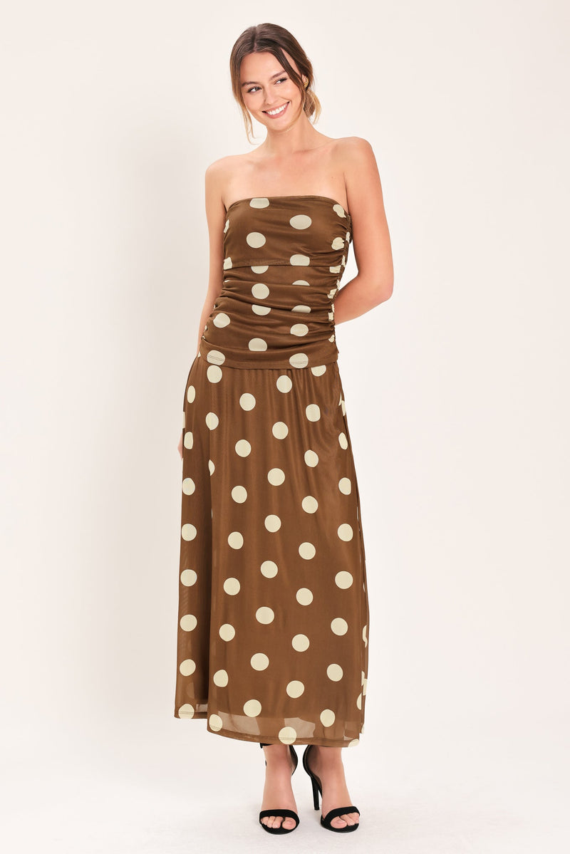 Woman wearing a brown strapless dress with white polka dots on a white background