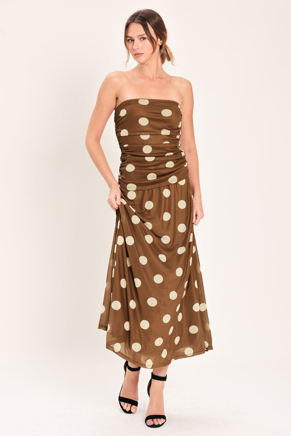 Woman wearing a brown strapless dress with white polka dots on a white background