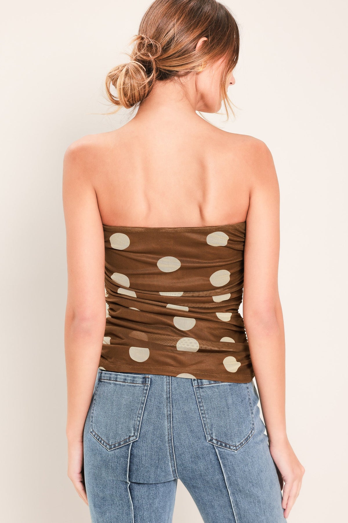 Woman wearing a strapless top with polka dots and jeans on a plain background