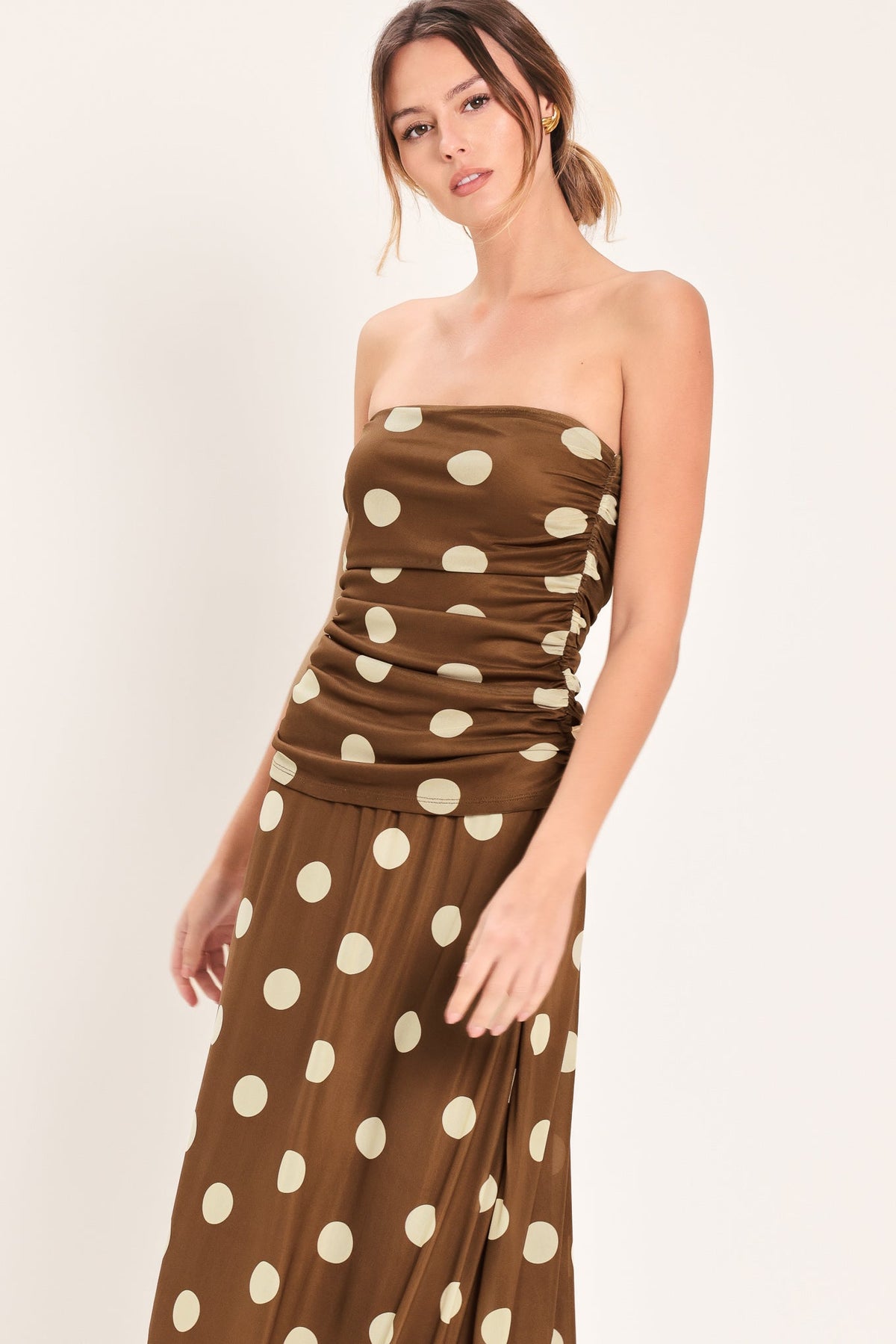 Woman wearing a brown strapless dress with white polka dots on a white background