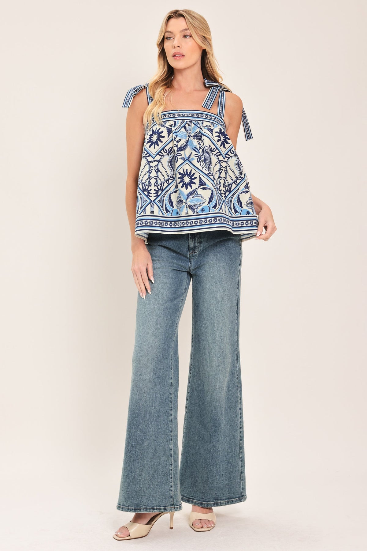 Woman wearing a blue and white patterned top with flared jeans on a white background