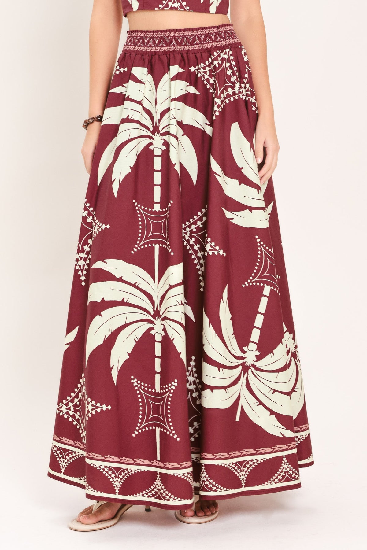 Long maroon skirt with white palm tree pattern worn by a person on a white background
