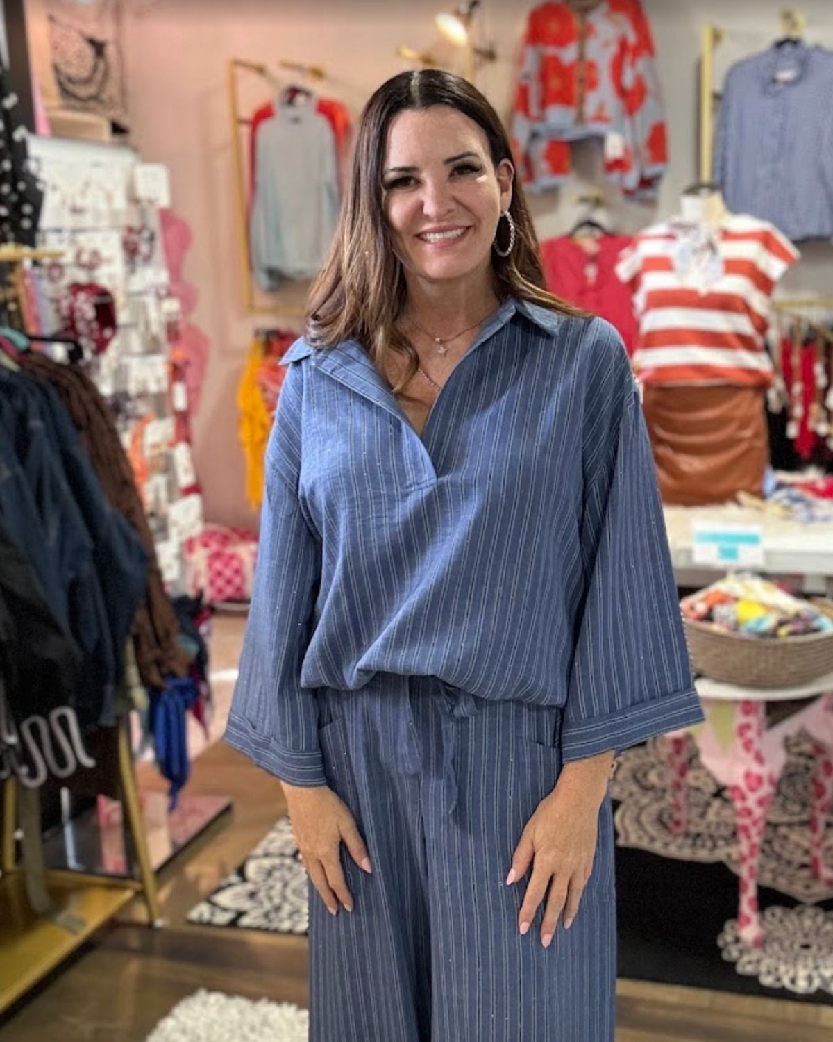 A woman wearing a blue and navy vertically striped wrap shirt and matching wide-leg pants, standing inside a clothing boutique.