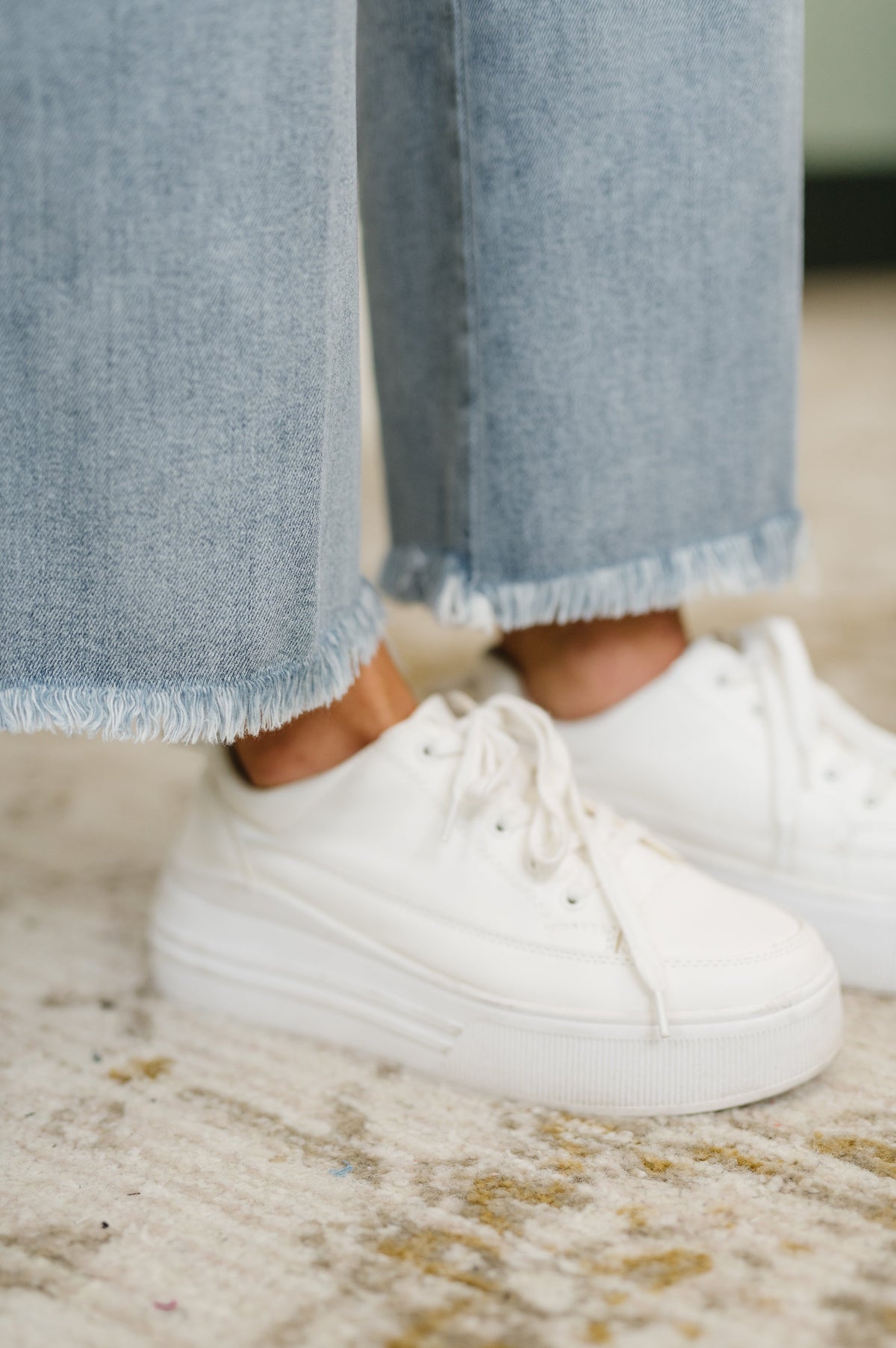 White sneakers worn with light blue jeans on a patterned carpet