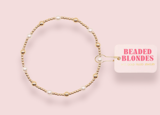Gold beaded necklace with a 'Beaded Blondes' tag on a pink background