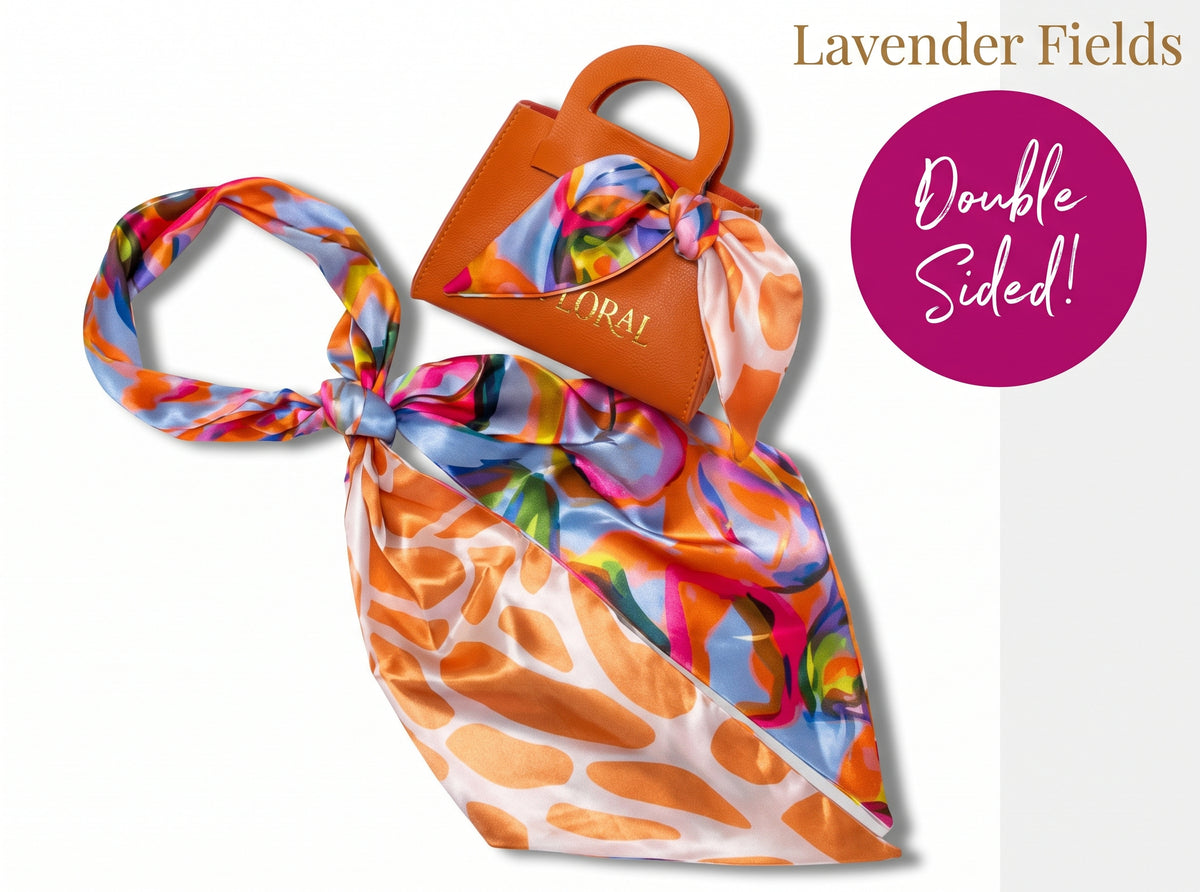 A double-sided silk scarf by Lavender Fields featuring a vibrant multicolor abstract print in orange, pink, blue, yellow, and green on a white base. The scarf is styled with one end tied in a knot and draped over a small orange handbag, set against a clean white background with promotional text overlays.