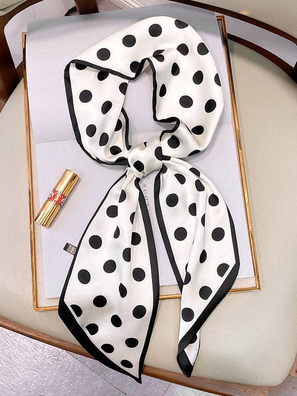 Black and white polka dot scarf on a white surface with a gold tube of lipstick.