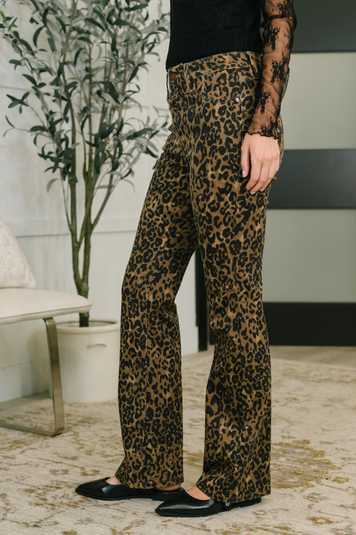 Person wearing leopard print pants in a room with a plant and furniture.