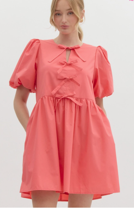 A woman modeling a pink mini dress with bubble sleeves, elastic cuffs, and a ribbon detail at the front.