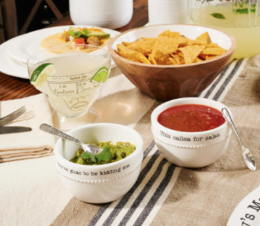 Dessert bowls with ice cream, fruit, and a spoon on a striped tablecloth.