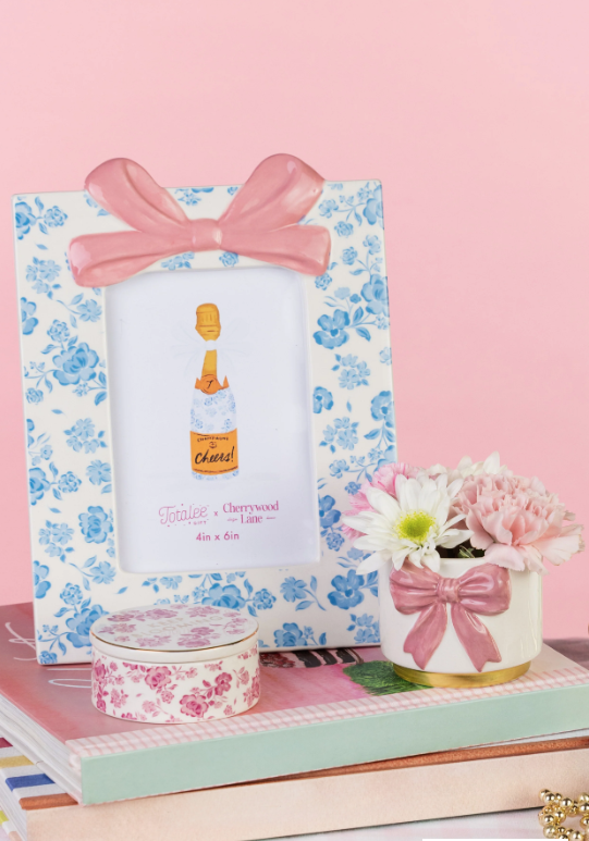 Floral photo frame with a pink bow, bottle illustration, and small floral arrangement on a pink background.