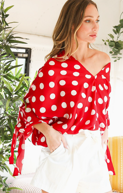 Woman wearing a red polka dot top with plants in the background
