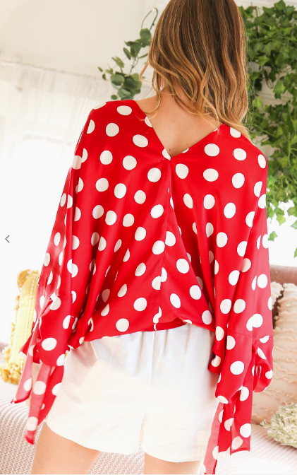Person wearing a red polka dot top with white shorts in an outdoor setting