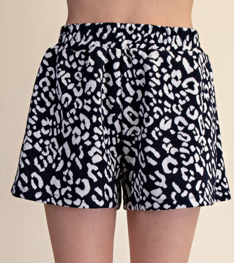 Black shorts with white leopard print pattern worn by a person on a beige background