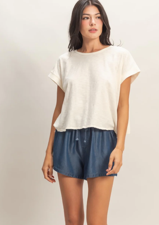 Woman wearing a white top and blue shorts on a plain background
