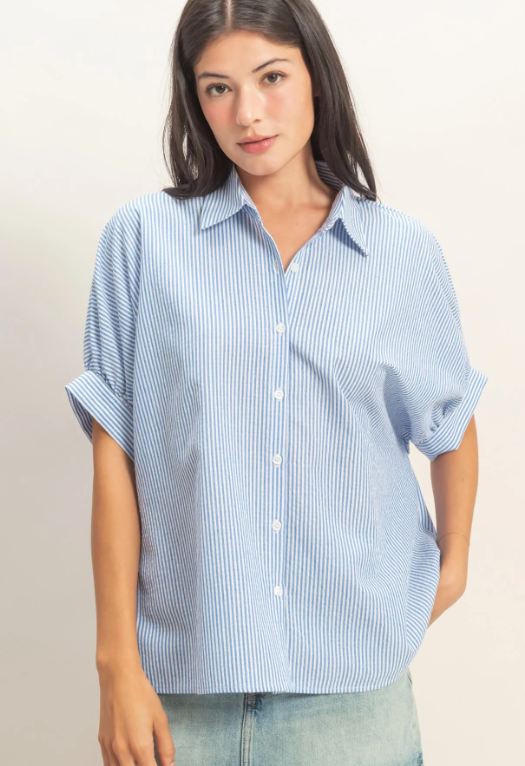 Woman wearing a light blue striped shirt and denim shorts on a plain background