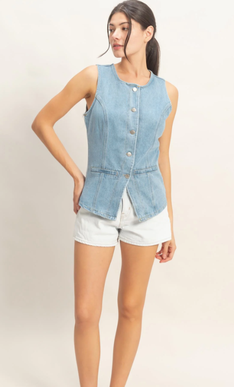 Woman wearing a denim vest over a white top and shorts on a plain background