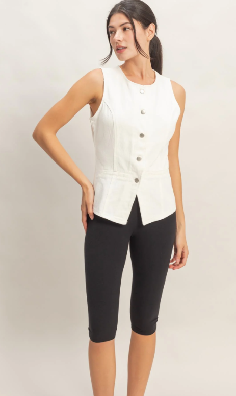 Woman wearing a white sleeveless blazer and black shorts on a light background
