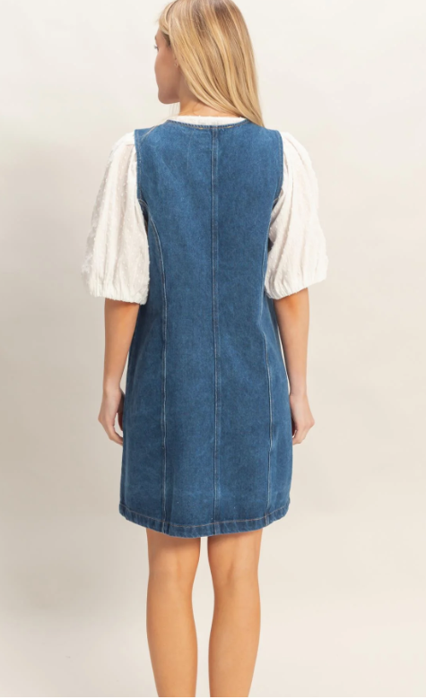 Woman wearing a denim dress over a white shirt on a plain background