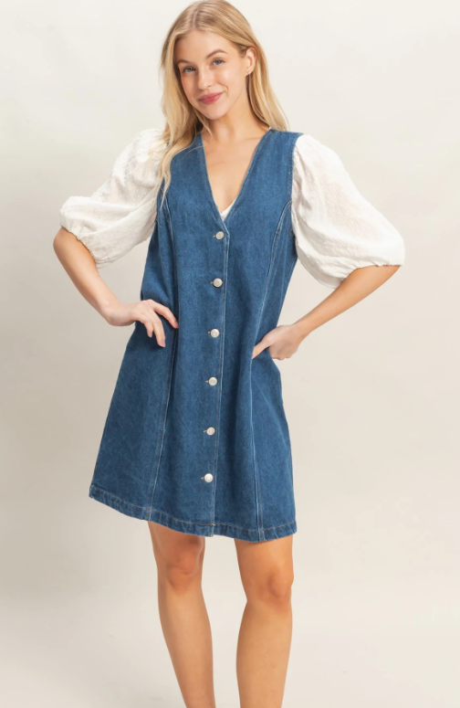 Woman wearing a blue denim dress over a white blouse on a plain background