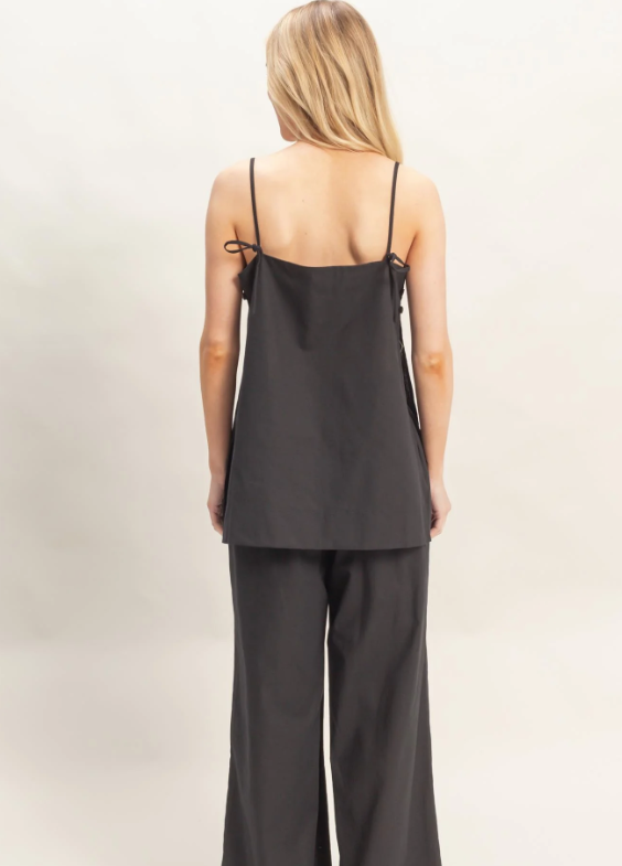 Woman wearing a black sleeveless top and pants on a beige background