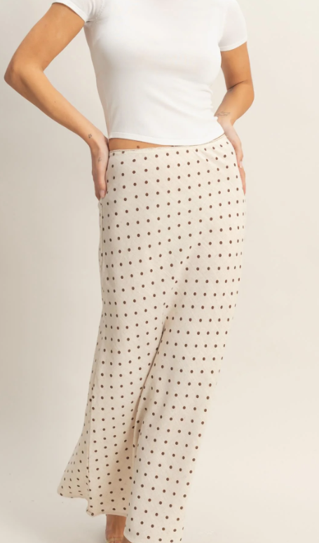 Person wearing a white t-shirt and beige polka dot skirt on a plain background