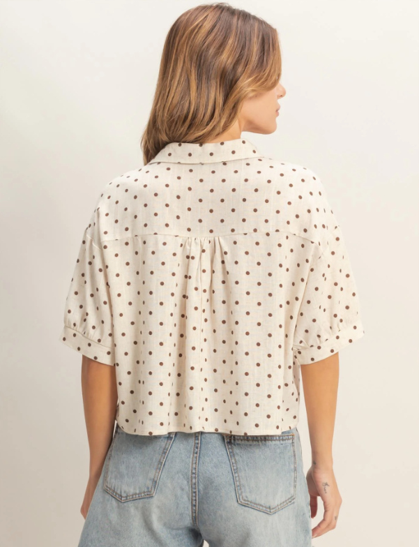 Woman wearing a polka dot blouse and jeans against a plain background