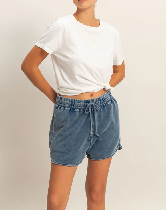 Person wearing a white t-shirt and blue denim shorts on a plain background