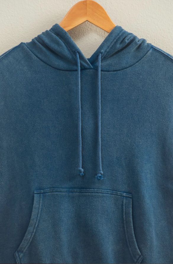 Blue hoodie on a wooden hanger against a beige background
