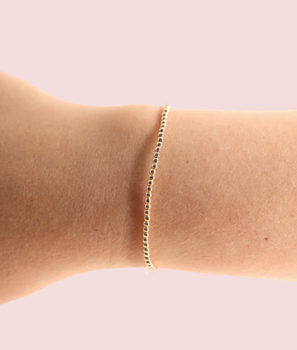 Gold bracelet on a person's wrist against a light pink background