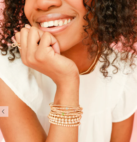 Woman wearing multiple gold bracelets on her wrist with a blurred background