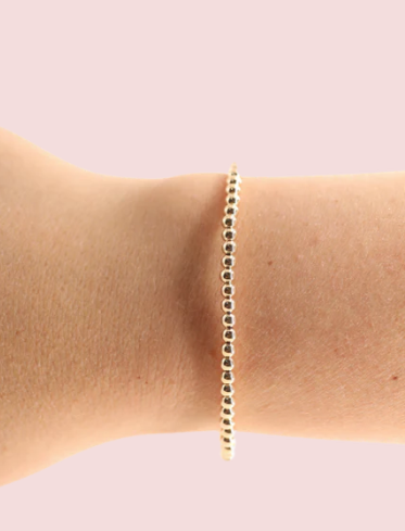 Gold bracelet on a person's wrist against a light pink background