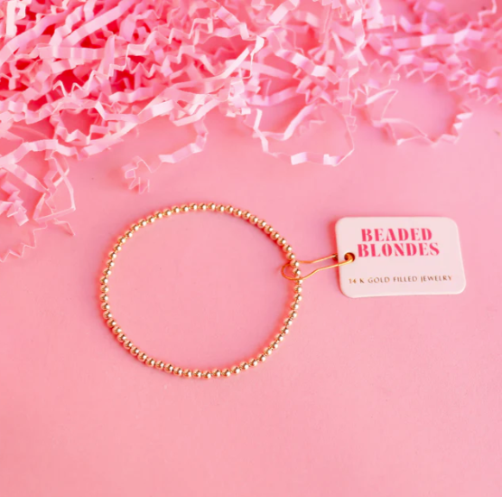 Gold beaded bracelet with a 'Beaded Blondes' tag on pink crinkled paper