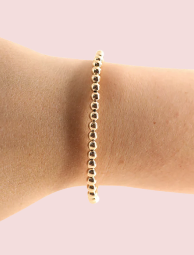 Gold beaded bracelet on a wrist against a light pink background