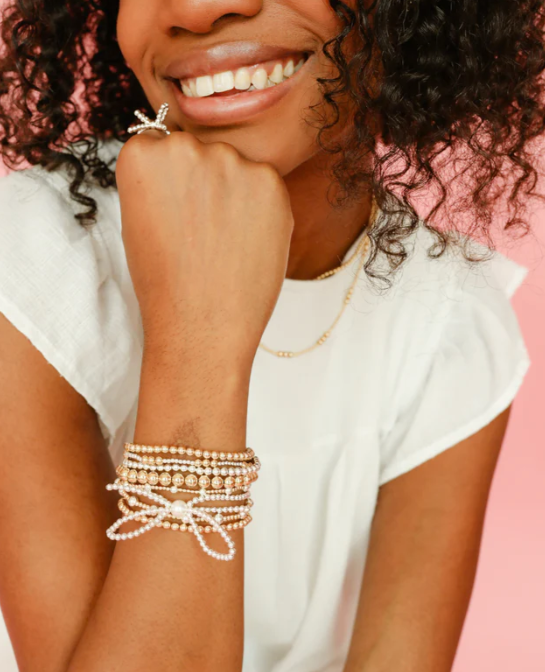 Woman wearing multiple pearl bracelets on a pink background