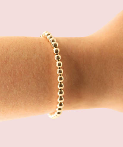 Gold beaded bracelet on a wrist against a light pink background