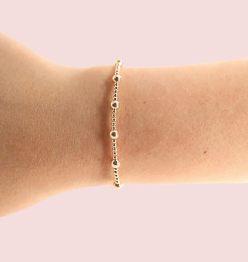 Gold bracelet on a wrist against a light pink background