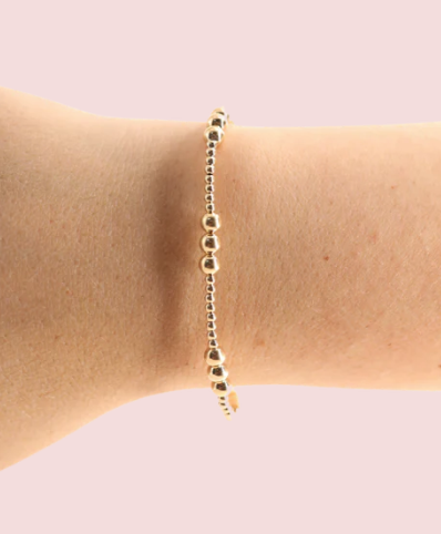 Gold bracelet on a wrist against a light pink background