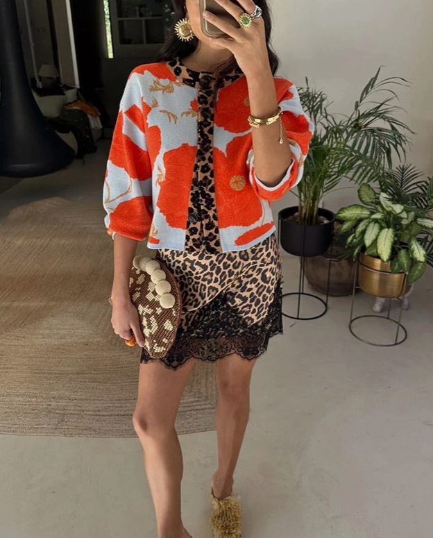 A woman takes a mirror selfie wearing a vibrant orange, white, and black abstract print jacket with leopard-print and black lace hem, holding a woven clutch.