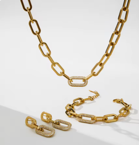 Gold chain jewelry set including a necklace, bracelet, and earrings, featuring elongated links with pavé-set clear stones, displayed on a clean white background.