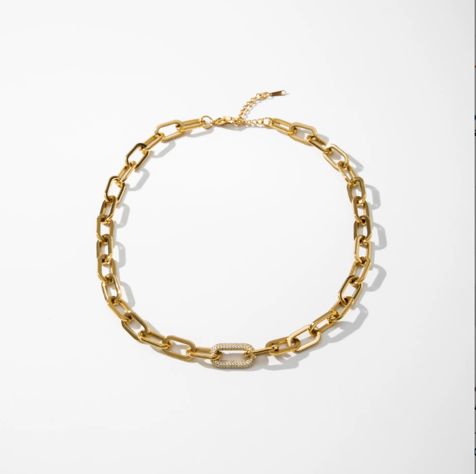 A gold chain necklace with a chunky, elongated link design and a central oval link featuring a textured pavé detail, displayed on a clean white background.