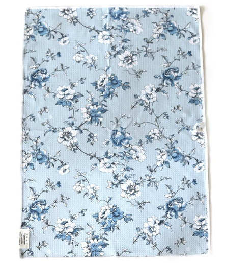 A square fabric item, likely a tea towel or hand towel, featuring a delicate blue and white floral pattern on a light blue background.