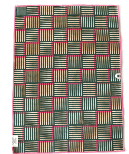 A square textile product, likely a towel or blanket, featuring a woven geometric pattern of dark green, beige, and bright pink stripes. The item is laid flat against a white background with a small white tag visible on the bottom left.