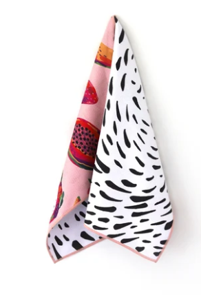 A folded square fabric accessory, likely a pocket square or scarf, featuring a split design: one side is light pink with colorful fruit illustrations, and the other is white with black irregular spots, set against a plain white background.