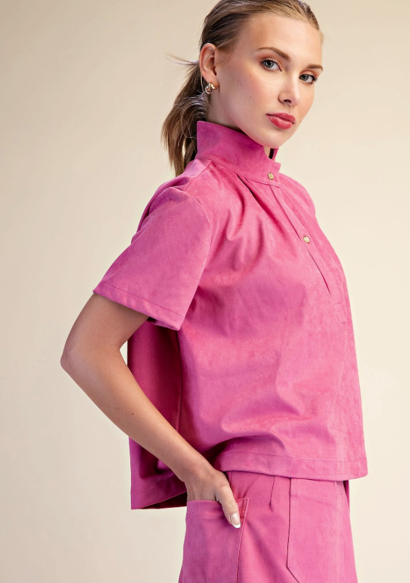 A woman modeling a bright pink short-sleeve scrub top and matching scrub pants against a plain beige studio background.