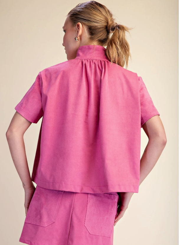 A woman shown from the back wearing a bright pink short-sleeve scrub top and matching pink bottoms against a plain beige studio background.