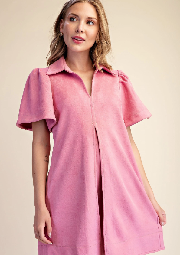 A woman wearing a pink short-sleeve collared dress with puff sleeves and a front button placket, photographed against a plain beige studio background.