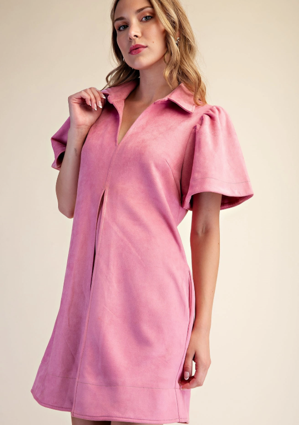 A woman wearing a pink short-sleeve collared dress with puff sleeves and a front slit, photographed against a plain beige studio background.
