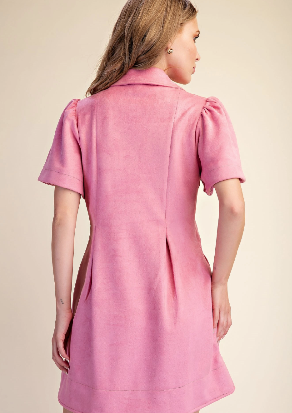 A woman shown from the back wearing a pink short-sleeve dress with puffed sleeves and a structured collar, photographed against a plain warm beige studio background.